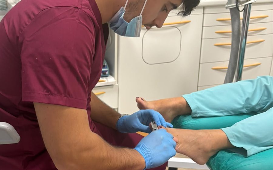 Alberto Saiz Zárate, con guantes y mascarilla, tratando la uña de un paciente en la camilla de podología